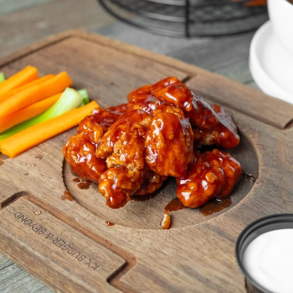 KX Burger + Beyond's boneless wings with BBQ sauce, carrots, celery, and ranch on a wooden board.