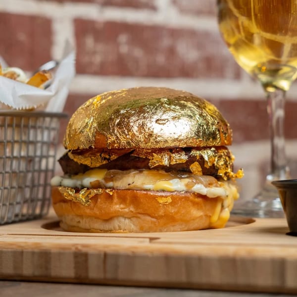 A KX Burger + Beyond burger with a gold leaf bun, fries, and a drink on a wooden board.