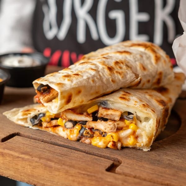 Two quesadillas filled with chicken, corn, black beans, and melted cheese on a wooden board.