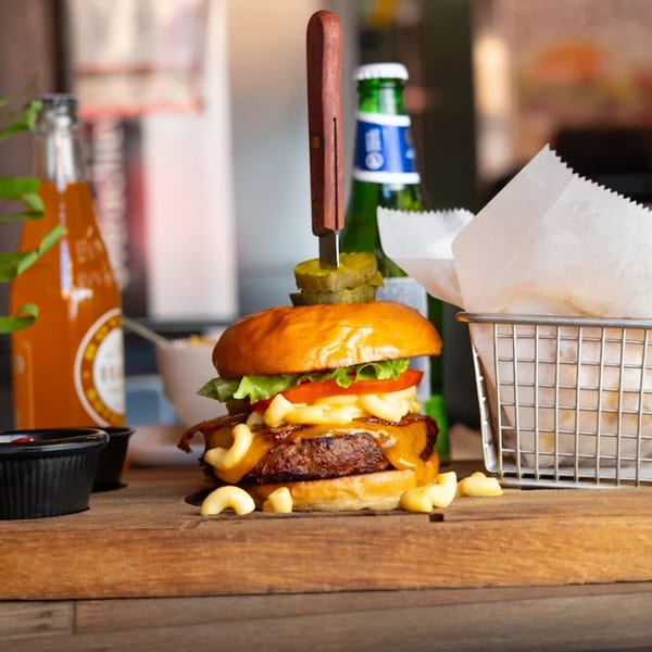 A KX Burger + Beyond burger with mac and cheese, bacon, lettuce, and tomato, served with fries and drinks.