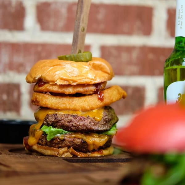 A double cheeseburger with onion rings, lettuce, and a pickle on a wooden board.