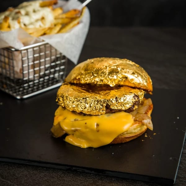 A KX Burger with a gold leaf bun, melted cheese, and caramelized onions, with fries in the background.