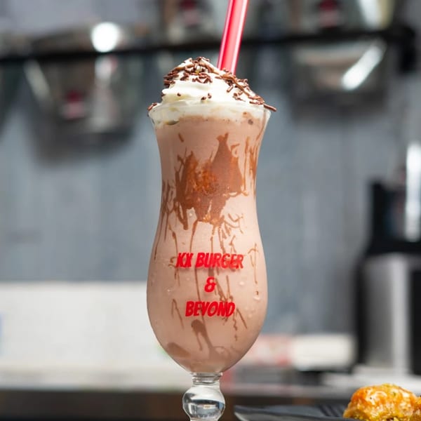 A KX Burger + Beyond chocolate milkshake with whipped cream, sprinkles, and a red straw.